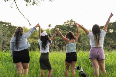 Dört Latin kız gökyüzüne yükselirken el ele tutuşuyorlar, özgürlüklerini ve güçlerini kutluyorlar.