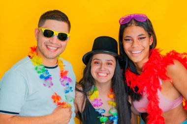 Sarı arka planda parti kıyafetleri içinde gülümseyen üç genç Latin. karnaval konsepti.