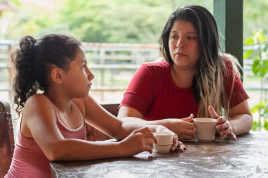 Genç Latin bir anne, Kolombiya 'da bir çiftlikte kahve içerken genç kızıyla çok ciddi konuşuyor..