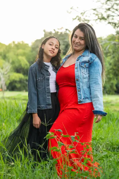Yeşil bir geçmişi olan, çimenli bir alanda poz veren Latin anne ve kız..