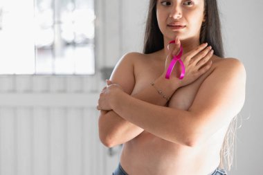 Latin bir kadın pembe bir kurdele tutarken göğüslerini elleriyle kapatıyor. Kanserle savaş