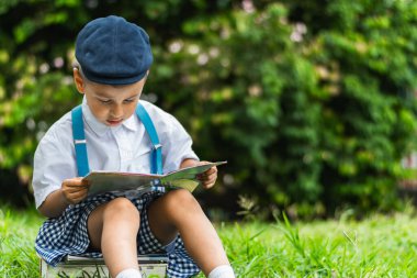 Küçük Latin çocuk parkta kitap okuyor, kitaplar üzerinde oturuyor ve konsantre oluyor..
