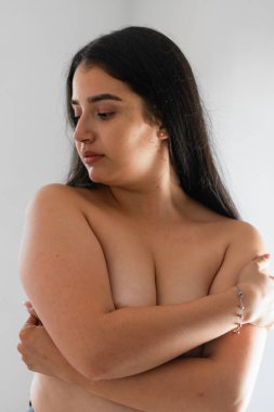 Beyaz bir arka planda göğüslerini elleriyle kapatan Latin bir kadın.