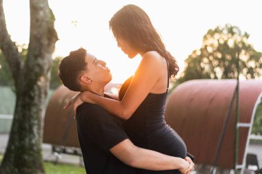 Genç Latin bir adam kız arkadaşını tutarken, kız ona sırılsıklam aşık, günbatımı ise arka planda.