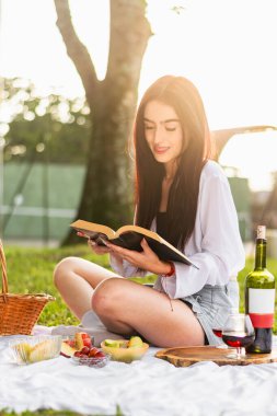 Çok mutlu ve gülümseyen ince latin kız arka planda altın bir günbatımı olan bir kitap okuyor.