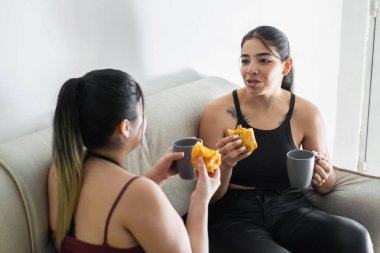 İki genç Latin arkadaş, evdeki kanepede oturup atıştırmalıklarını yerken konuşuyorlar..