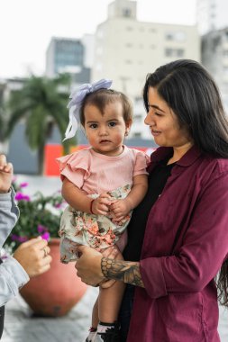 Genç Latin bir anne kucağında. Küçük kızı da ileriye bakıyor..