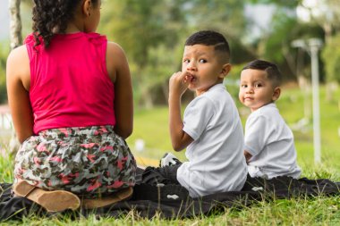 Parkta oturan iki erkek ve bir kızın arkasını görmek, Latin çocukların geriye bakması, dönüp bakmaları
