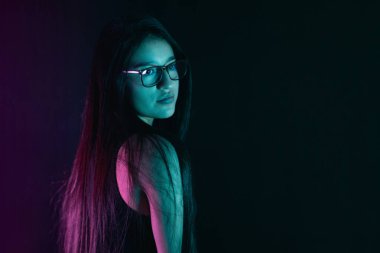 Genç Latin bir kadın, renkli ışıklarla bir stüdyo resmine poz verirken ciddi bir şekilde yan bakıyor..