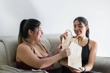 İki genç Latin kadın alışveriş yaptıktan sonra çok mutlular, hediye çantaları değiş tokuş ediyorlar.