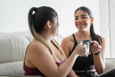 Genç Latin kadınlar kanepede oturur, kahve fincanlarıyla kadeh kaldırır, birbirlerinin gözlerine bakar ve gülümserler..