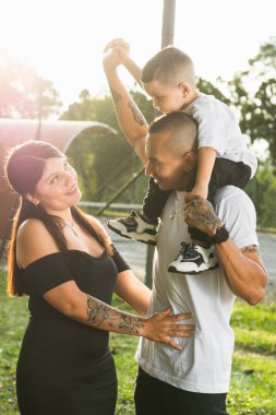 Genç Latin bir çift, çocukları ile parkta yürürken babasının omuzlarında taşıdığı mutlu Kolombiyalı aile.