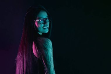 Genç Latin kadın gülümsüyor ve yan bakıyor, renkli ışıklarla bir stüdyo resmine poz veriyor..