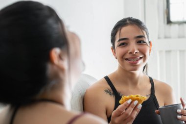 Genç Latin bir kadın arkadaşına bakıp gülerken, abur cuburunu yerken, diş teli takan bir kadın, diş konsepti ve ağız sağlığı