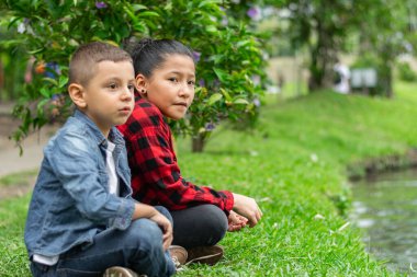 Parktaki gölün yanındaki çimlerde oturan çocuklar.