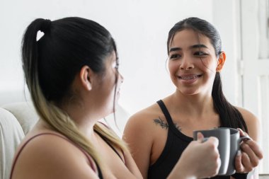 İki Latin kadının birbirine bakıp kahve fincanlarıyla kadeh kaldırırken gülümsemesi..