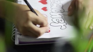 Asgari çalışma masasındaki spiral bir defterde harfleri engellemek için kırmızı renk ekleyen bir çocuğun görüntüsünü kapat.