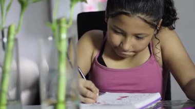 Okul çağındaki küçük kız, modern bir masa kurulumunda renkli kalemlerle renkli bloknotlar yazmaya odaklanmış..