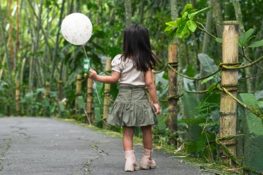Latin çocuk bambu kaplı hayvanat bahçesi yolunda beyaz balonu tutarak geri dönüyor..