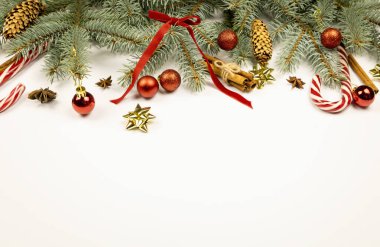 Yılbaşı ya da Noel süslemeleri. Noel ağacı dalları, kırmızı toplar, koniler, kırmızı kurdeleler ve fiyonklar, tarçın çubukları, anason yıldızları ve beyaz arka planda lolipop. Metin için yer
