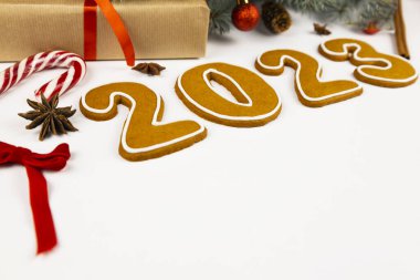 Beyaz arka planda 2023 numara. Yakınlarda Noel ağacı dalları, kırmızı toplar, koniler, kurdeleler, bir lolipop, tarçın ve yıldız anason var.
