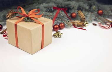 Beyaz arka planda Noel ağacı dalları, koniler ve Noel toplarının arka planında kırmızı kurdele bulunan el işi hediye kutusu. Kış tatili karşılama kavramı