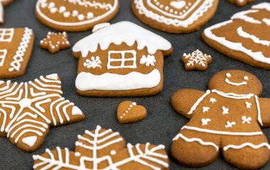 Ev şeklinde gri bir zemin üzerinde kremalı Noel kurabiyesi ve zencefilli adam, bir Noel ağacı ve toplar, yıldızlar ve kar taneleri ve kalpler. Kapat.