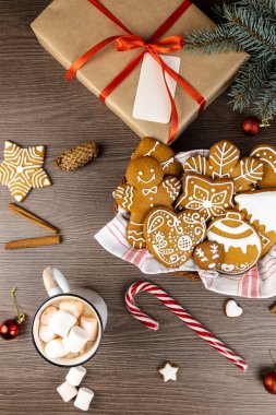 Noel konsepti. Bir fincan sıcak kakao, marşmelov, zencefilli kurabiye ve ahşap bir masanın üzerinde hediye kutusu. Noel dekoru. Yukarıdan görüntüle
