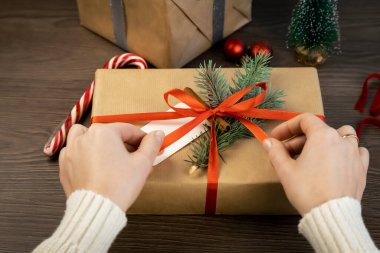 Kırmızı kurdeleyi hediye kutusuna bağlayan ellerin yakın çekimi