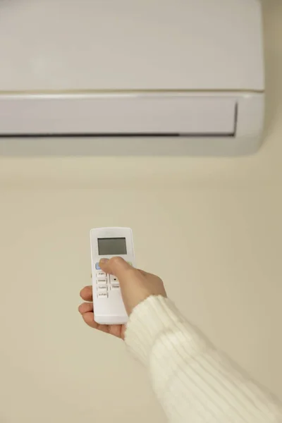 A womans hand is holding the air conditioner remote control. Air conditioner with remote control