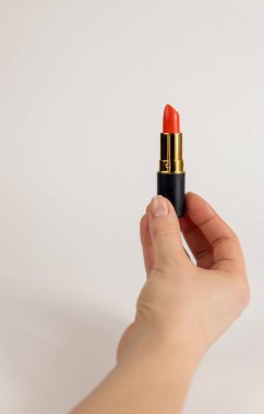 A womans hand holds red lipstick. Close up on a white background