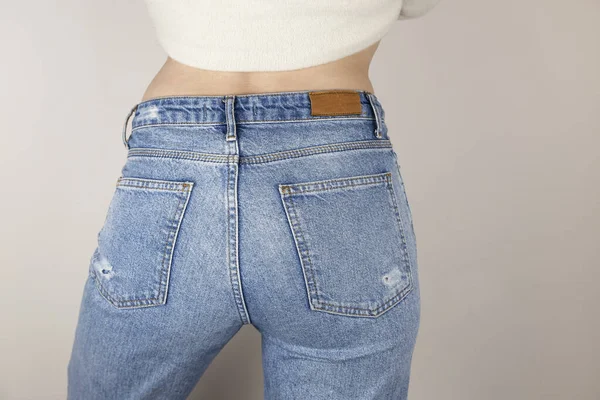Woman in jeans near white wall indoors, close-up, rear view. The woman put on jeans