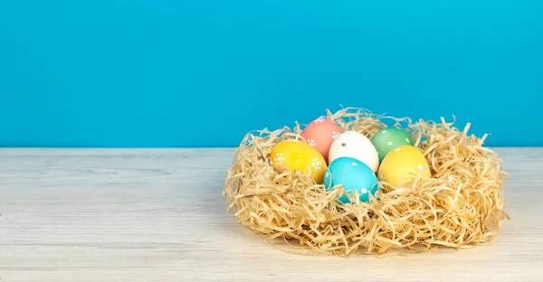 Painted Easter eggs in a nest on a blue background. Place for text. The concept of Easter holidays