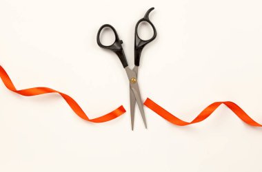 Beyaz arkaplandaki kırmızı saten kurdeleyi makasla kes. Yukarıdan görüntüle