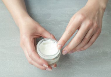 Kadın elleri gri arka planda kozmetik ürünü olan bir kavanozu tutuyor. Kapat. en üstteki görünüm