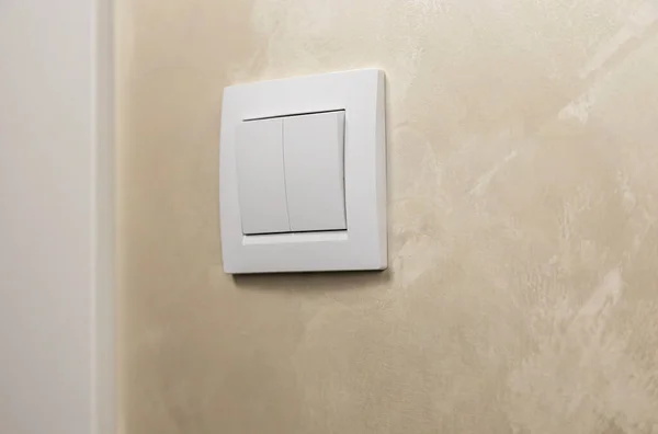 A plastic mechanical switch of white color on a light wall. Turn the lights off or on. The concept of saving electricity
