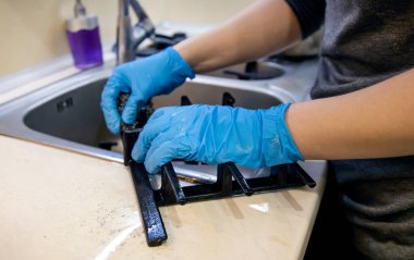 Mavi lastik eldivenli eller mutfaktaki dökme demir ızgarayı temizler.