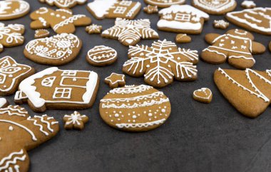 Zencefilli kurabiyeler, ev şeklinde gri arka planda krema ve zencefilli ekmek adam, ağaç ve top, yıldızlar ve kar taneleri ve kalpler.