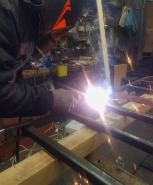 Bir işçi kaynak makinesi ve elektrot kullanarak metal bir yapıyı kaynaklıyor. Kaynaklı ürünler ve kaynakçılık kavramı