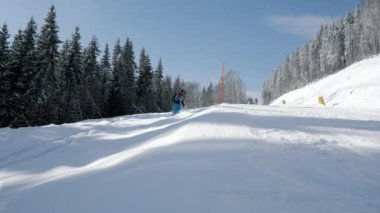 Bir kayak merkezinde yavaş çekimde yokuş aşağı giden snowboardcu, kameranın yanından geçiyor ve üzerine kar atıyor, kış dağlarında aktif dinleniyor.