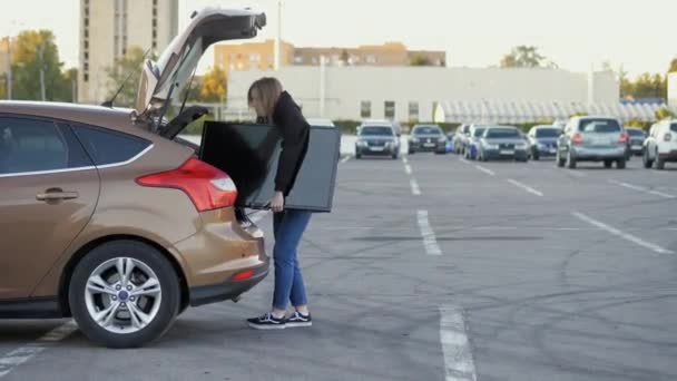 女性は近くのスーパーマーケットの駐車場で車のトランクの現代的なテレビを引き出します 配信コンセプト — ストック動画