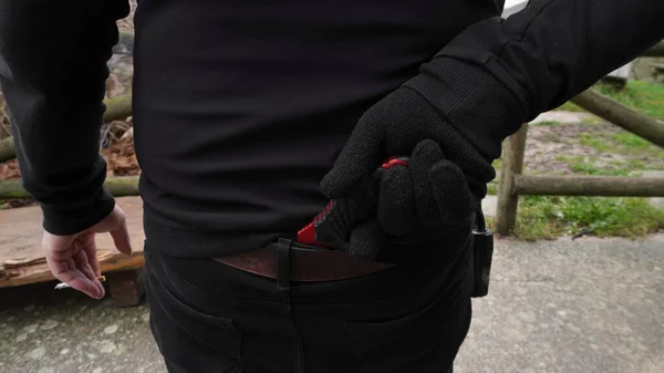 a person holds a knife hidden in his pants behind his back with his hand