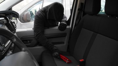        a man in a black hood steals a red wallet from a car                         
