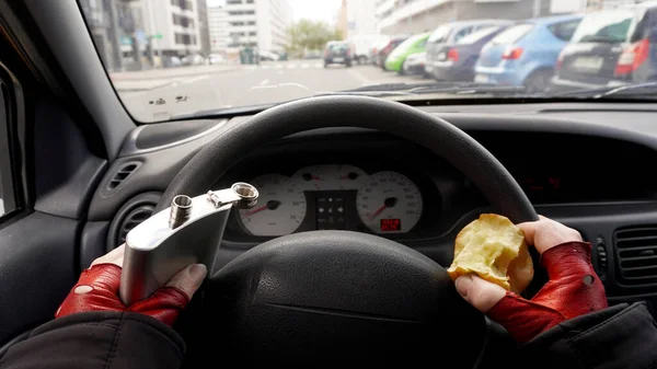 a woman in red gloves driving takes alcohol and eats an apple