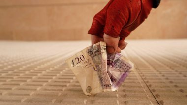 Kırmızı eldivenli bir el yerden 20 sterlin kaldırır.                                