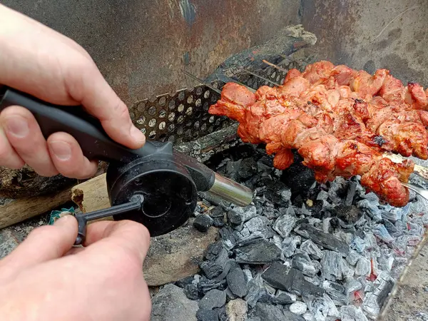 using a hand-held barbecue fan when cooking meat over charcoal