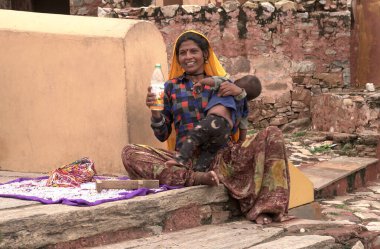 JAIPUR, INDIA 14 AĞUSTOS 2019: Çocuklu bir kadın Amber kalesinde oturuyor ve turistlere alfabe boncukları satıyor.