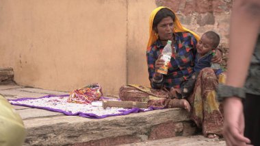 JAIPUR, INDIA 14 AĞUSTOS 2019: Çocuklu bir kadın Amber kalesinde oturuyor ve turistlere alfabe boncukları satıyor.