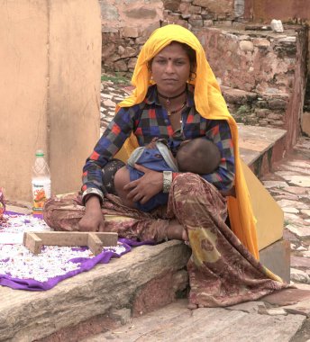 JAIPUR, INDIA 14 AĞUSTOS 2019: Çocuklu bir kadın Amber kalesinde oturuyor ve turistlere alfabe boncukları satıyor.