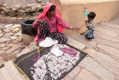 JAIPUR, INDIA 14 AĞUSTOS 2019: Çocuklu bir kadın Amber kalesinde oturuyor ve turistlere alfabe boncukları satıyor.